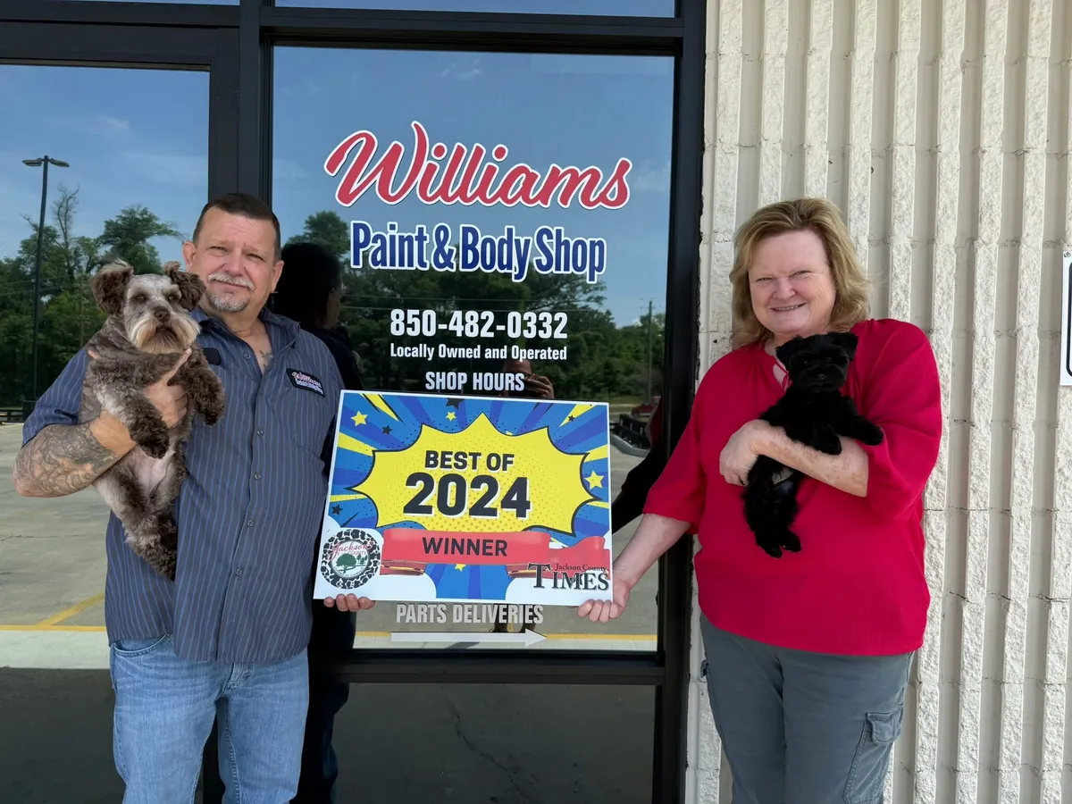 Eddie and Theresa Williams holding their dogs Coco and Sissy in front of Williams Paint & Body Shop