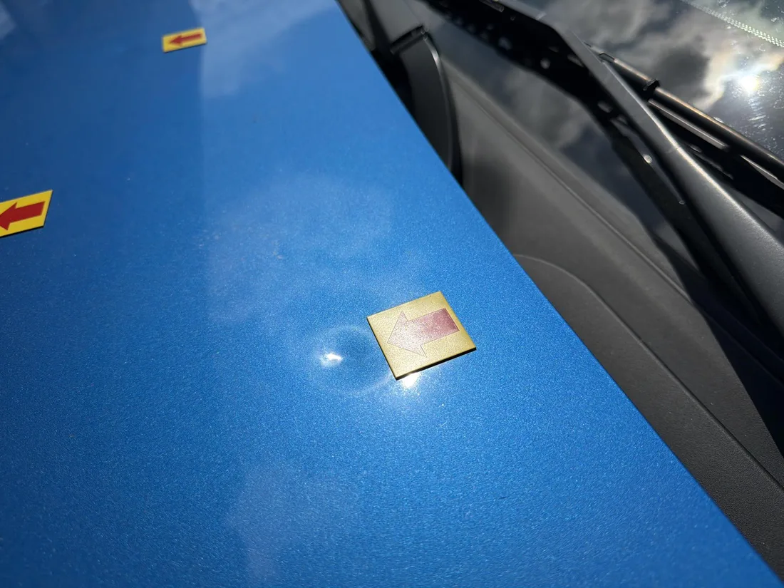Closer view of marked hail dents on the blue Nissan Sentra hood near the windshield.